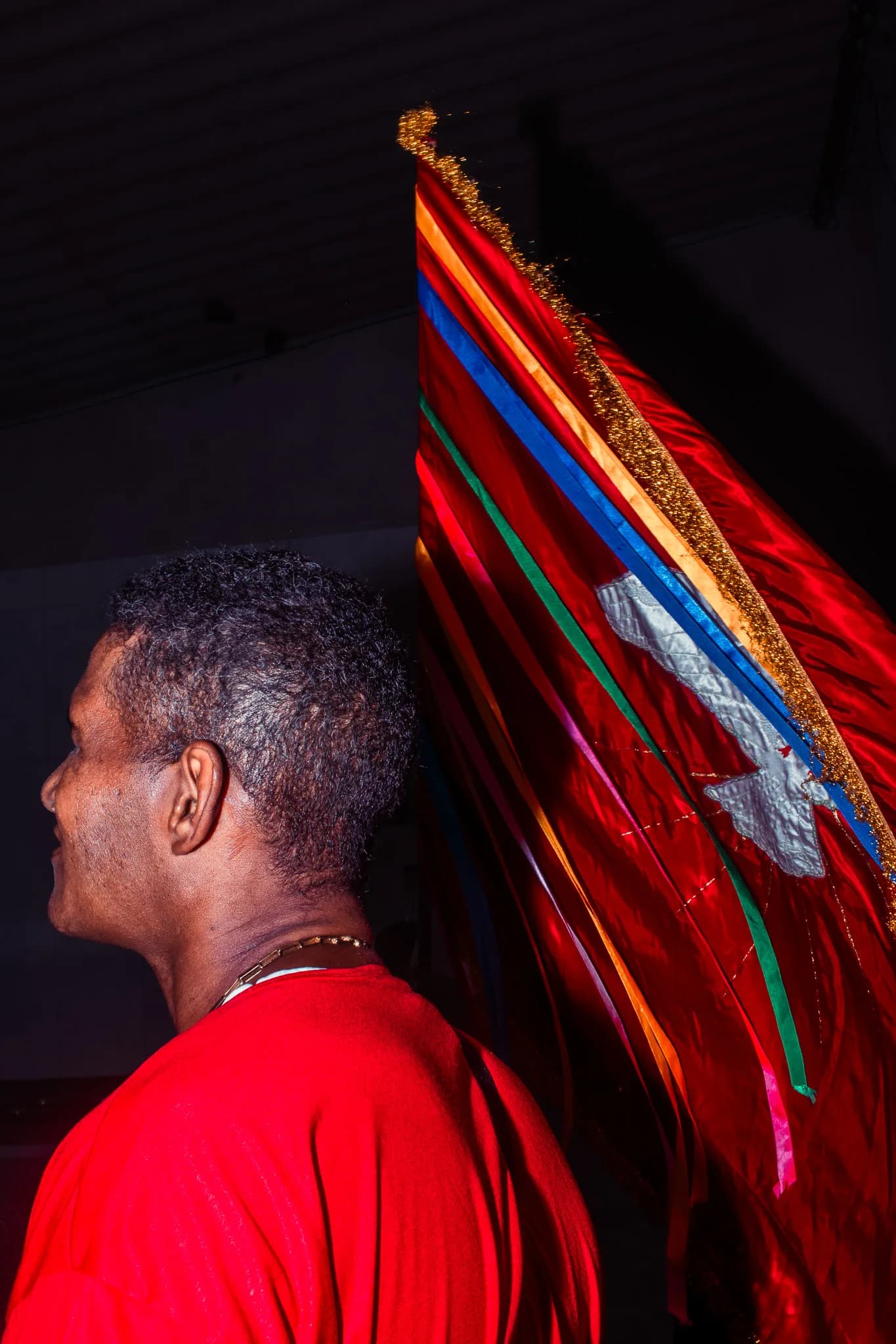 A man in a red shirt carries the ribboned banner of the Folia do Divino.