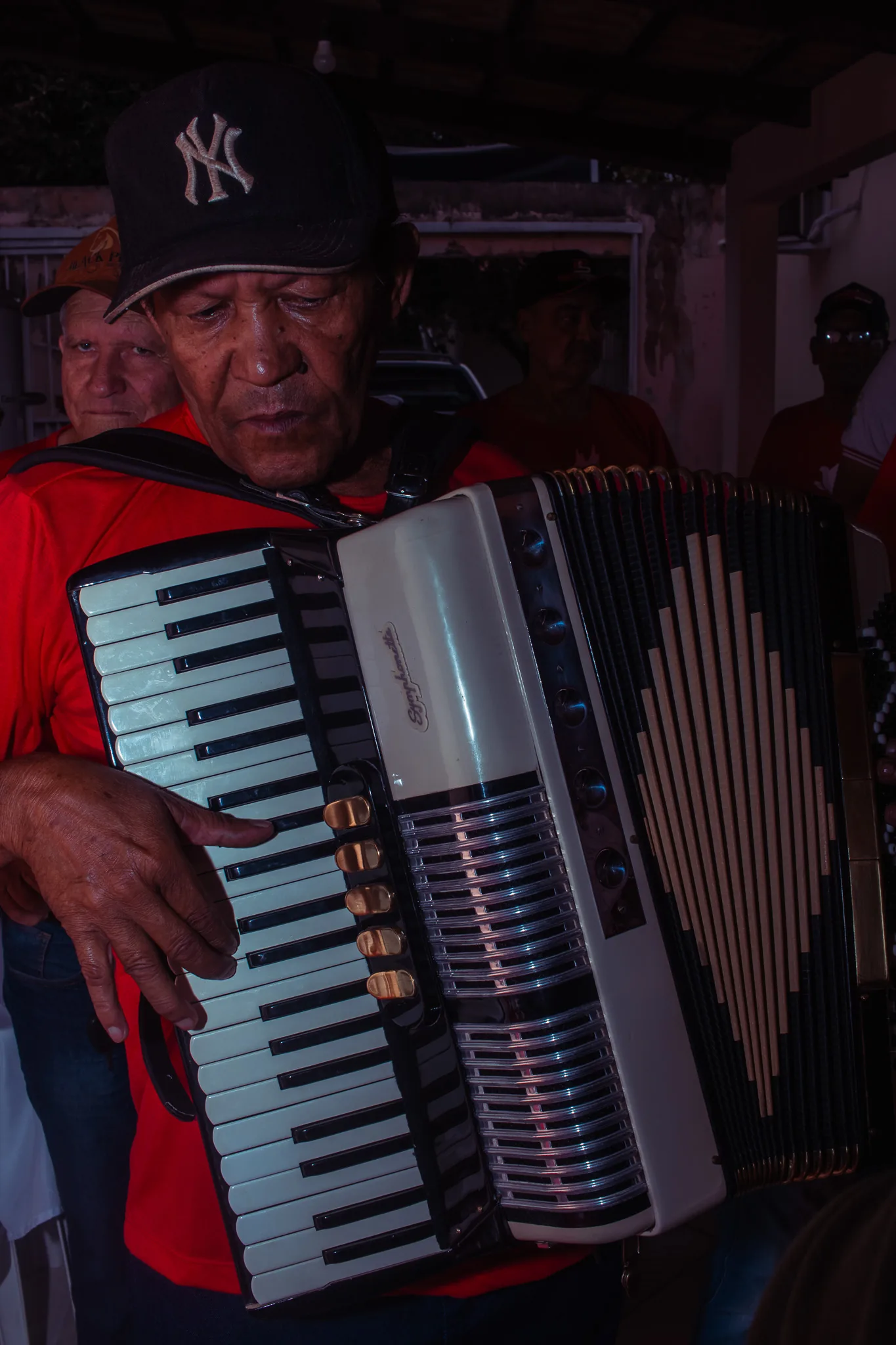 An accordion player in a cap, mid tune, inside the crowd of the feast.