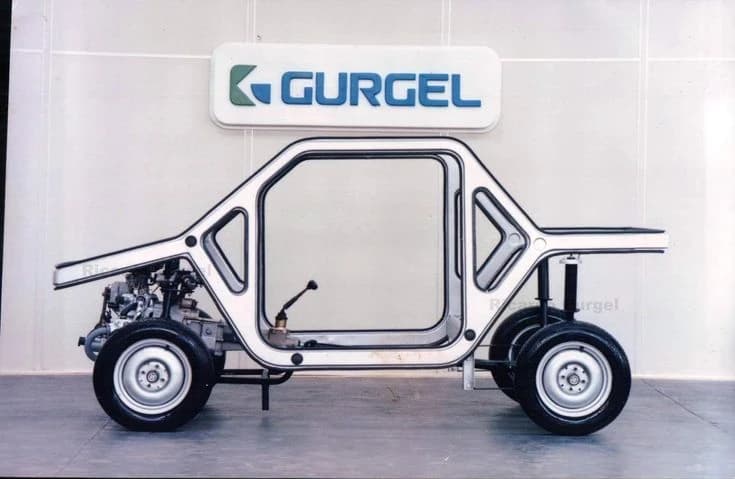 The bare chassis of a Gurgel on a stand, wheels and steering fitted, beneath the Gurgel wordmark.