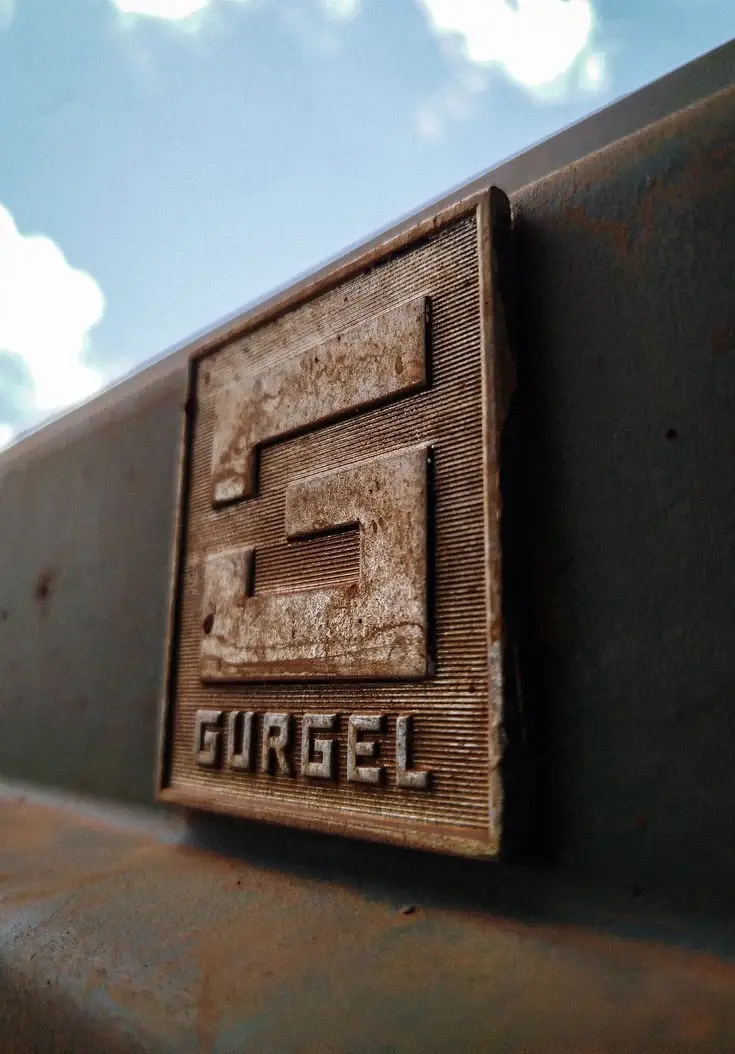Close-up of the cast Gurgel emblem on a rusted steel panel.