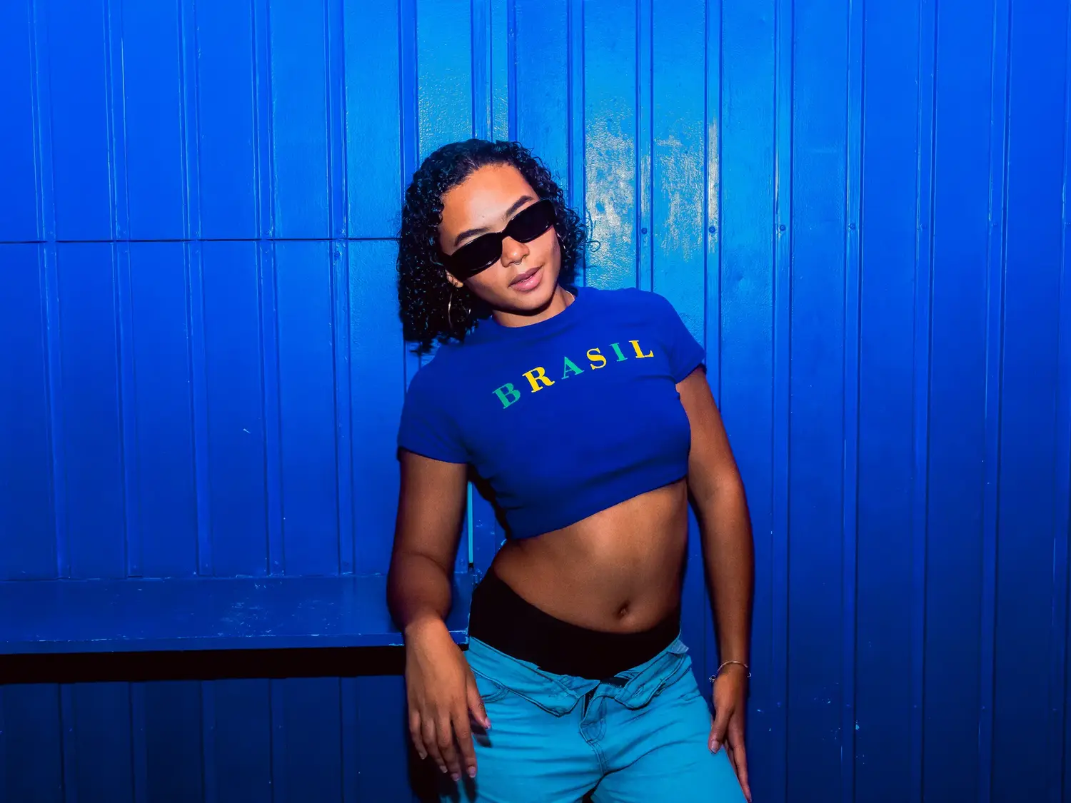 A guest posing against the blue wall in a Brasil shirt and sunglasses.