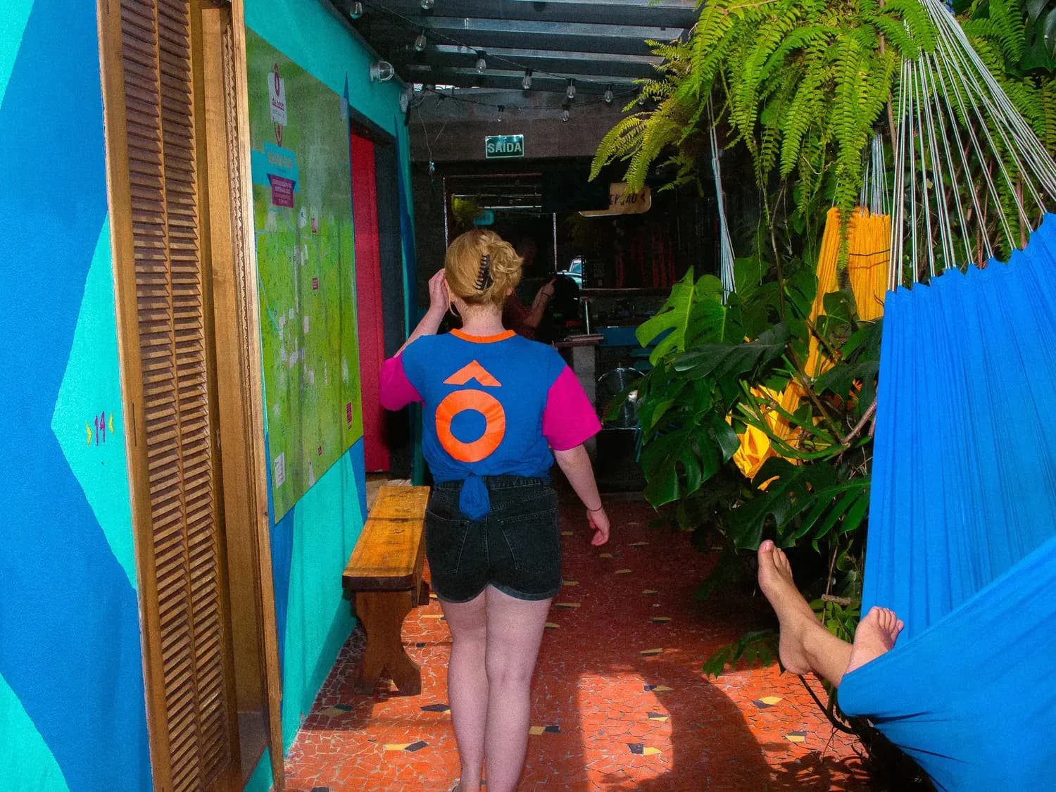 The planted corridor of the hostel, a guest walking through with a backpack.