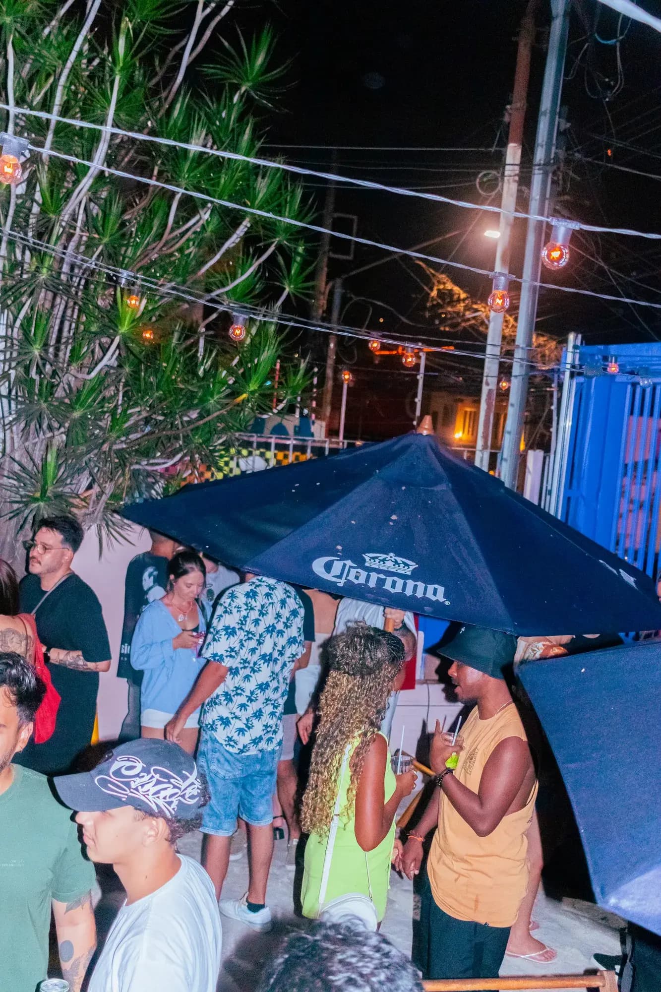 The street outside the hostel at night, people gathered under a bar umbrella.