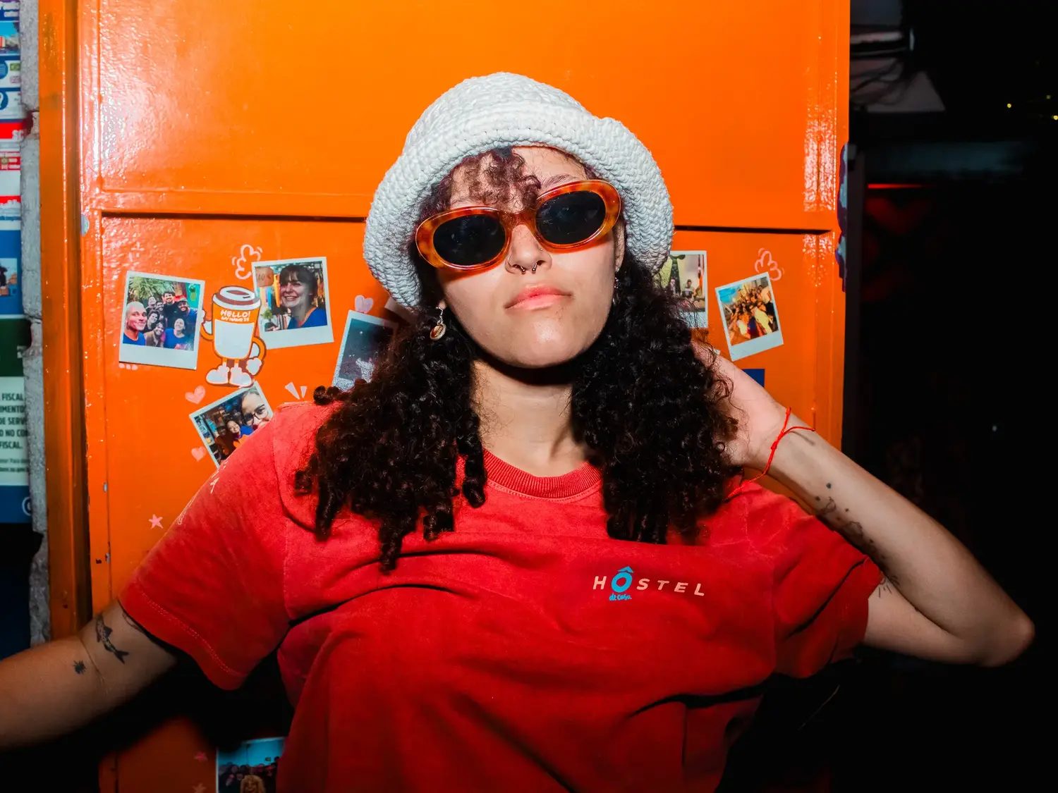 A staff member in the hostel shirt against the orange fridge covered in photographs.