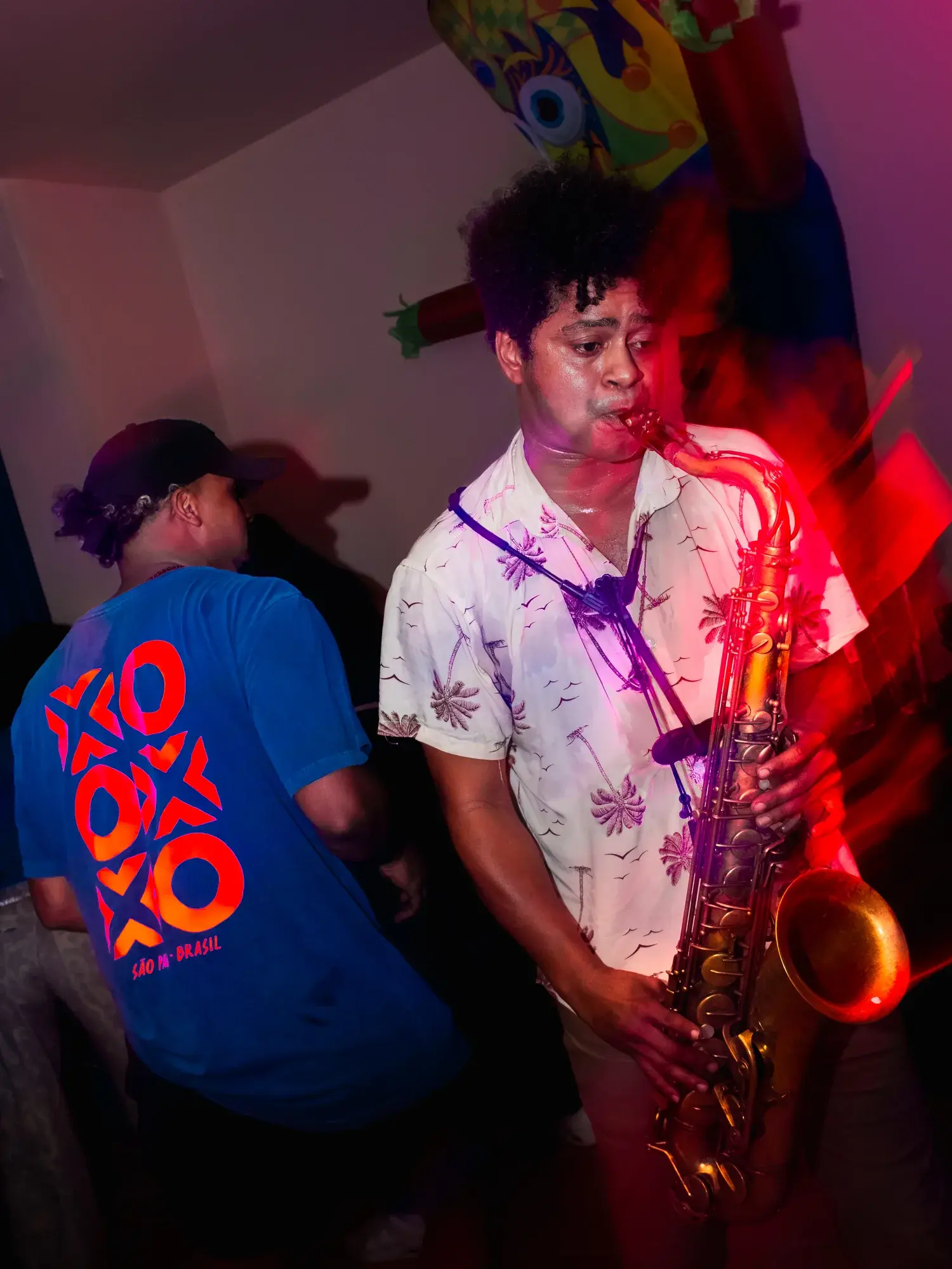 A saxophone player performing live in red light over the DJ deck.