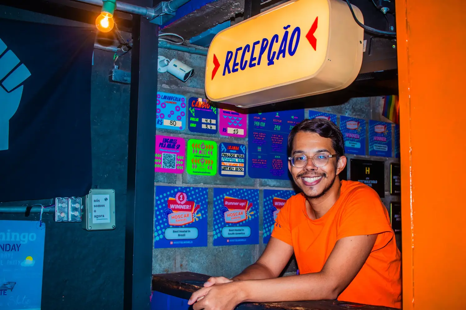 The Ô de Casa front desk under a lit RECEPÇÃO sign, a staff member smiling behind it.