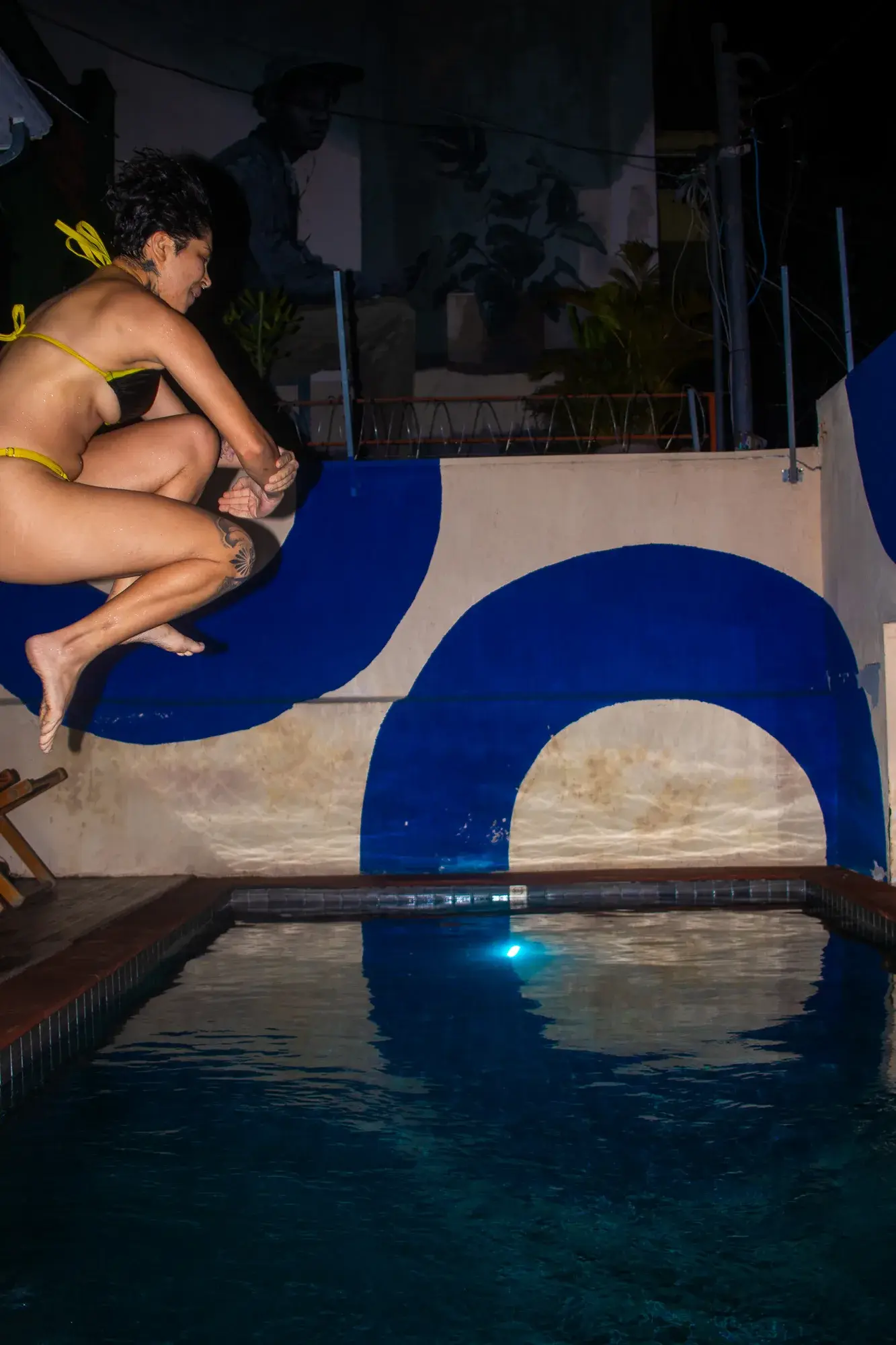 The lit pool at night, a guest sitting on the painted edge.